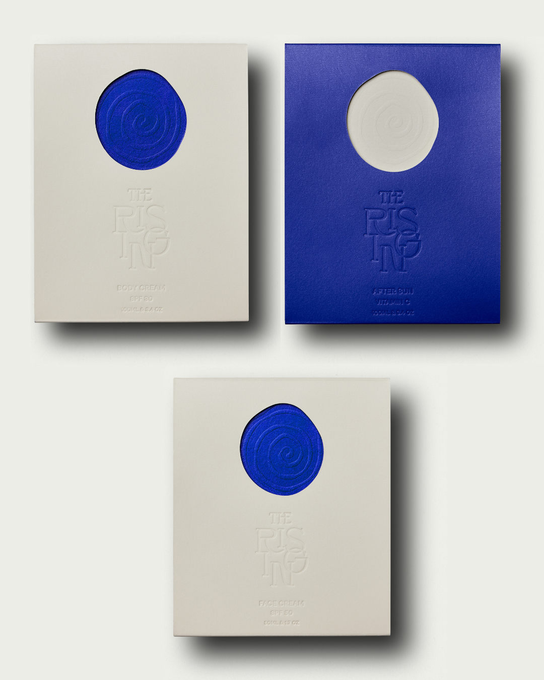 Three pebble-shaped bottles of suncare for face and body and after sun with 'The Rising' branding on a light gray background