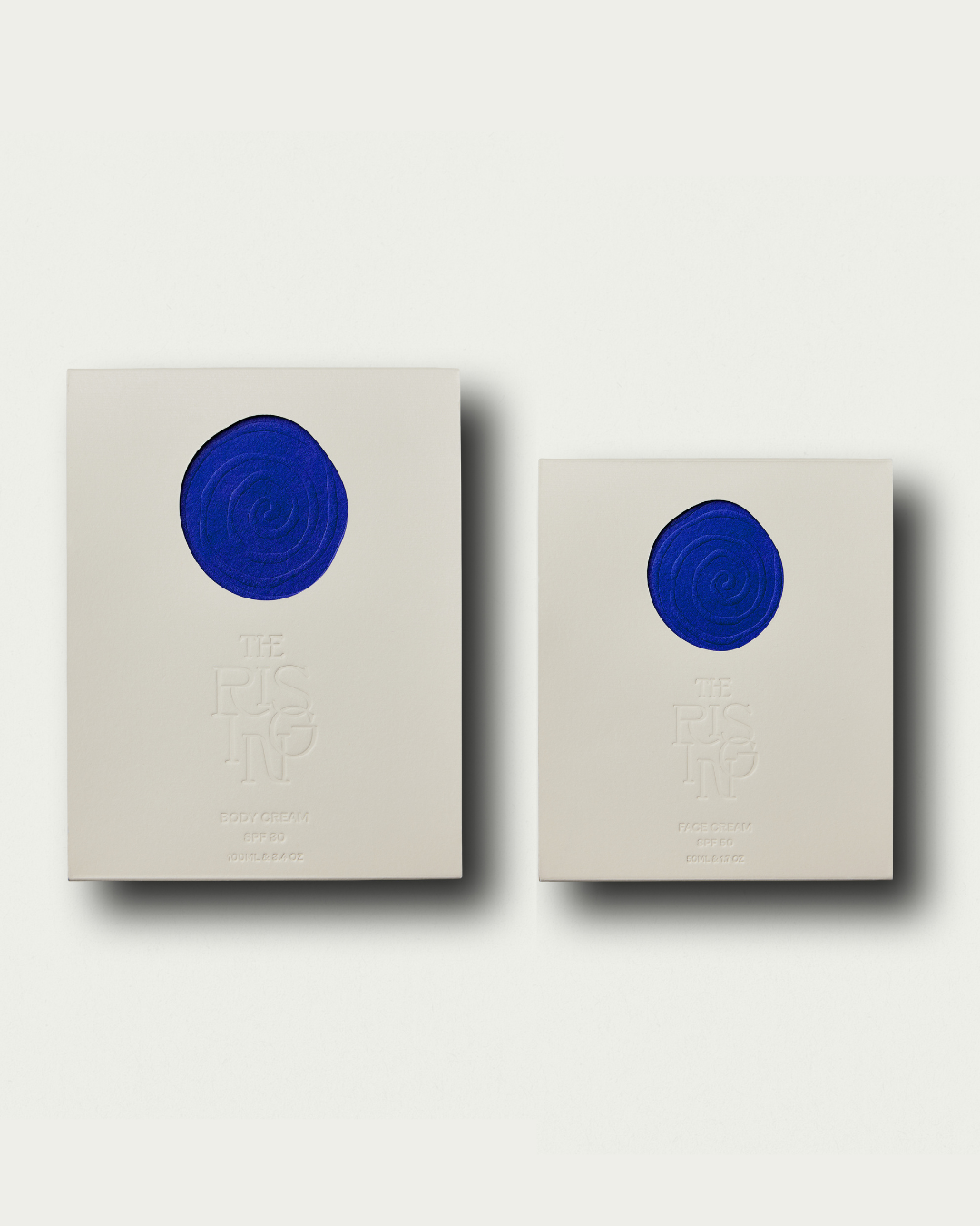 Two beige boxes for face and body spf cream with The Rising branding designs on a white background