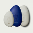 Three pebble-shaped bottles of suncare for face and body and after sun with 'The Rising' branding on a light gray background