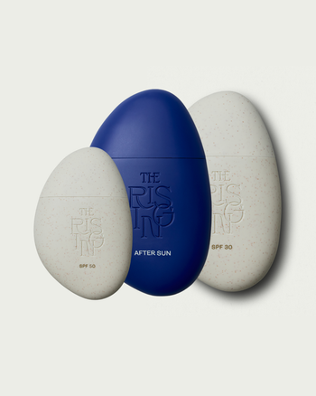 Three pebble-shaped bottles of suncare for face and body and after sun with 'The Rising' branding on a light gray background