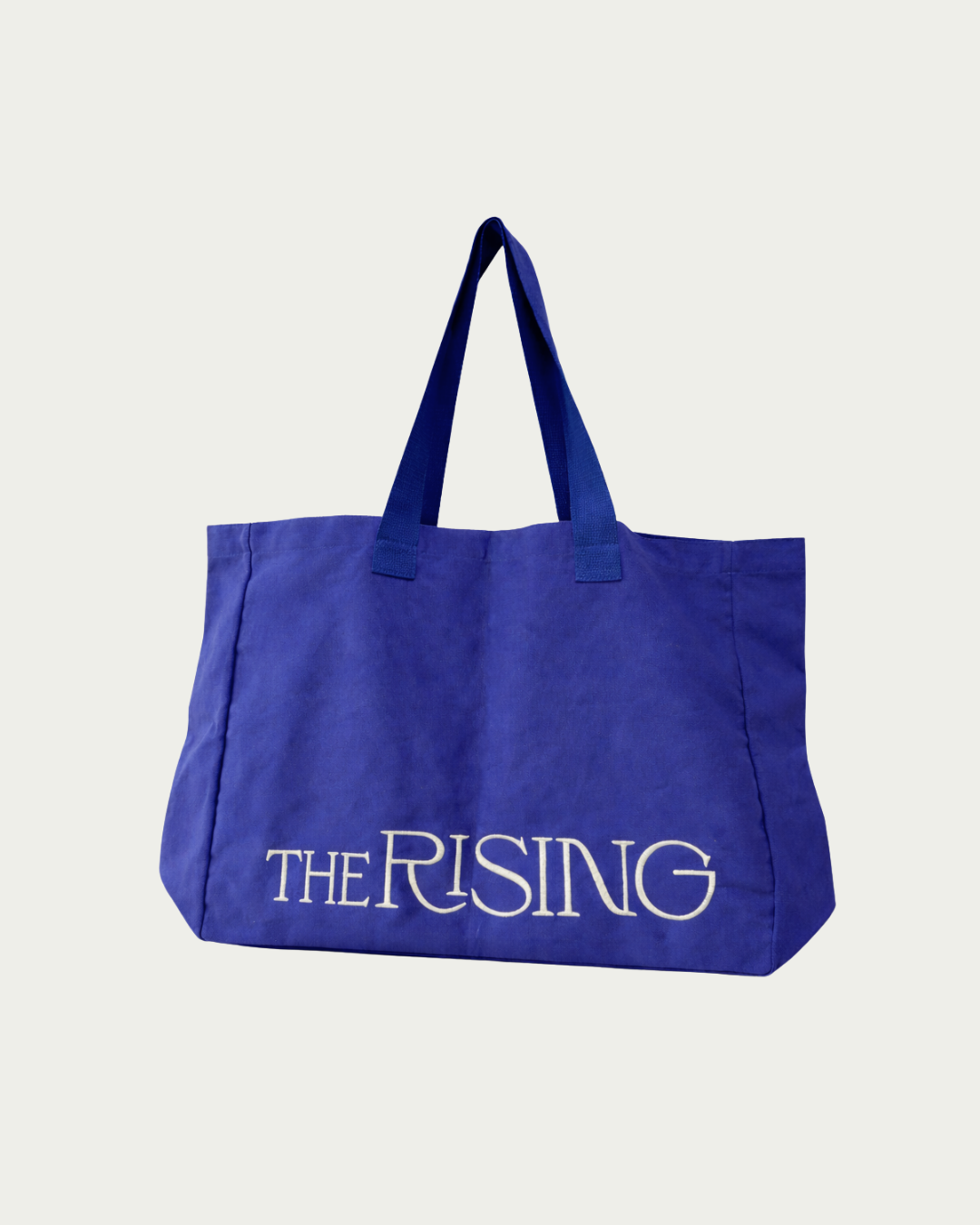 Blue tote bag with 'The Rising' text on a light gray background